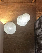 Three off-white woven Clérachic pendant lights lit at different heights in front of a tall brick wall.