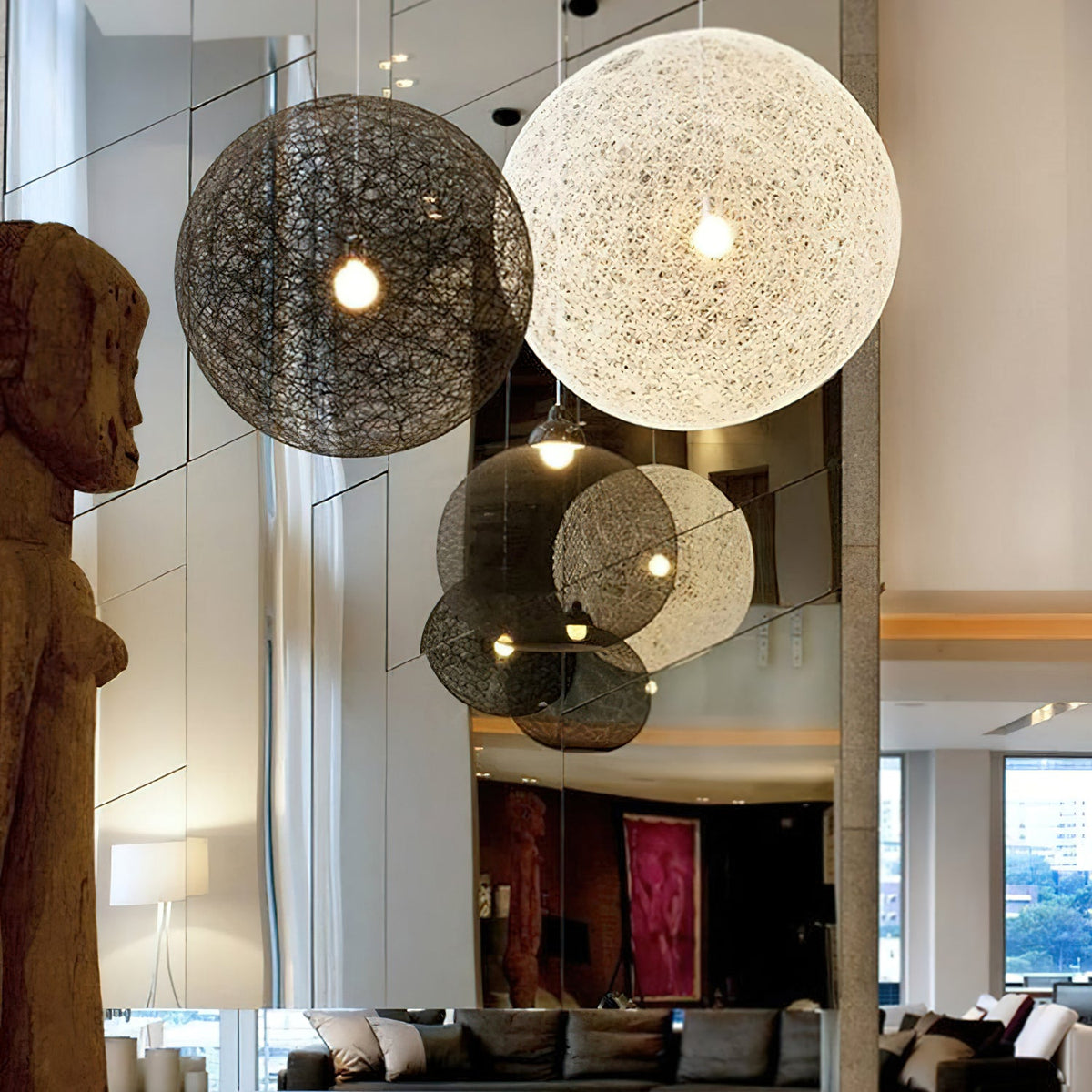 A black and an off-white woven Clérachic pendant light lit in a double-height room, with their reflections in a mirrored wall.