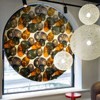 Off-white woven Clérachic pendant lights of different sizes in front of a large round window with a patterned panel.