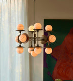 The Clérachic Xenon chandelier lit beside sheer curtains and a green artwork, its alabaster globes glowing amber.
