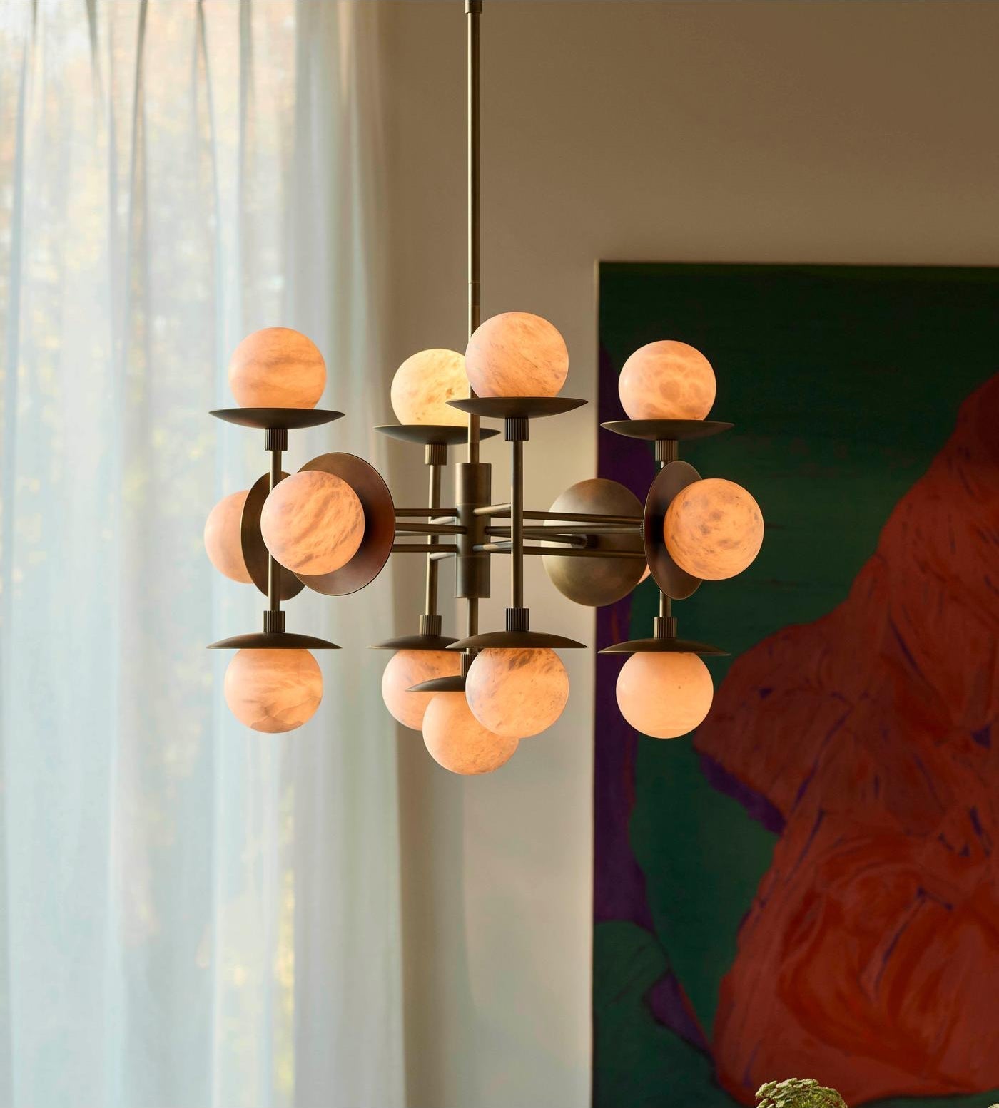 The Clérachic Xenon chandelier lit beside sheer curtains and a green artwork, its alabaster globes glowing amber.