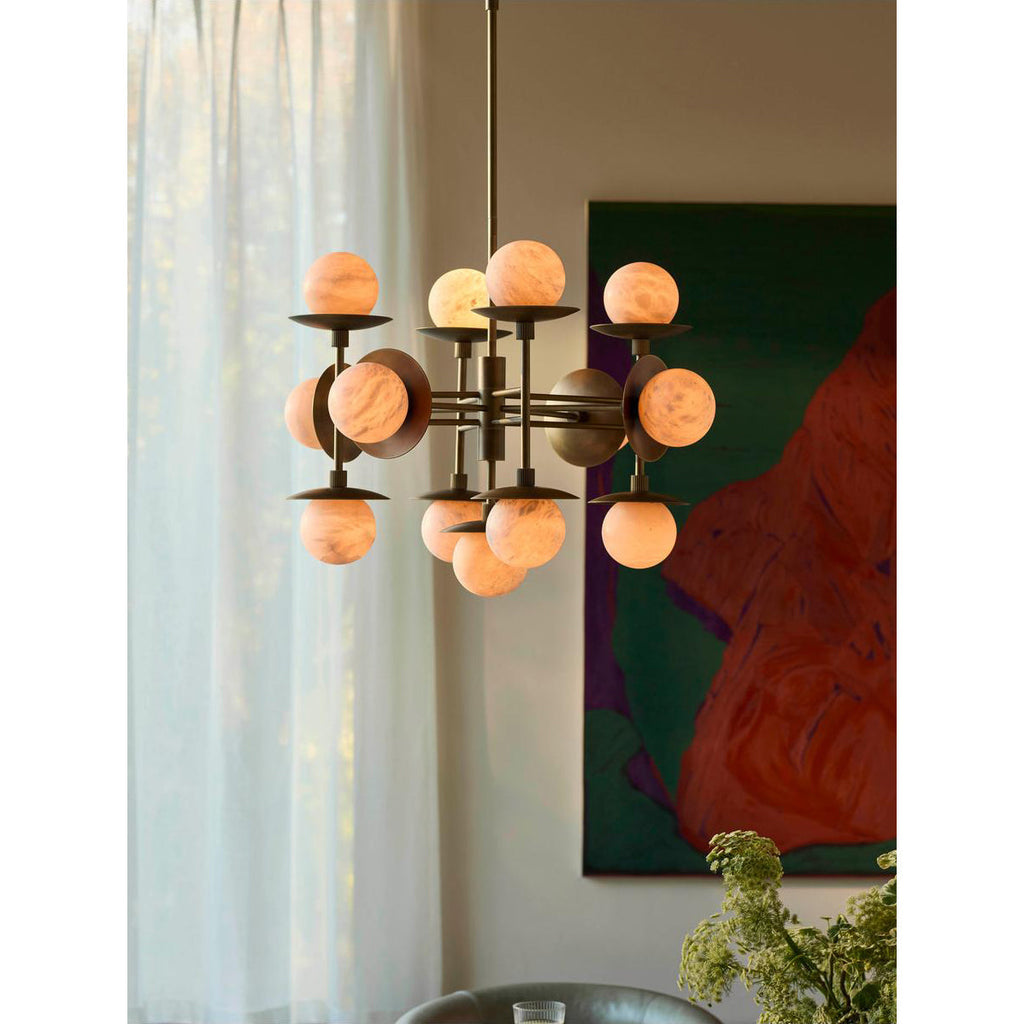 Clérachic Xenon chandelier seen from further back, the brass frame silhouetted against daylight through linen curtains.