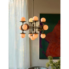 Clérachic Xenon chandelier seen from further back, the brass frame silhouetted against daylight through linen curtains.