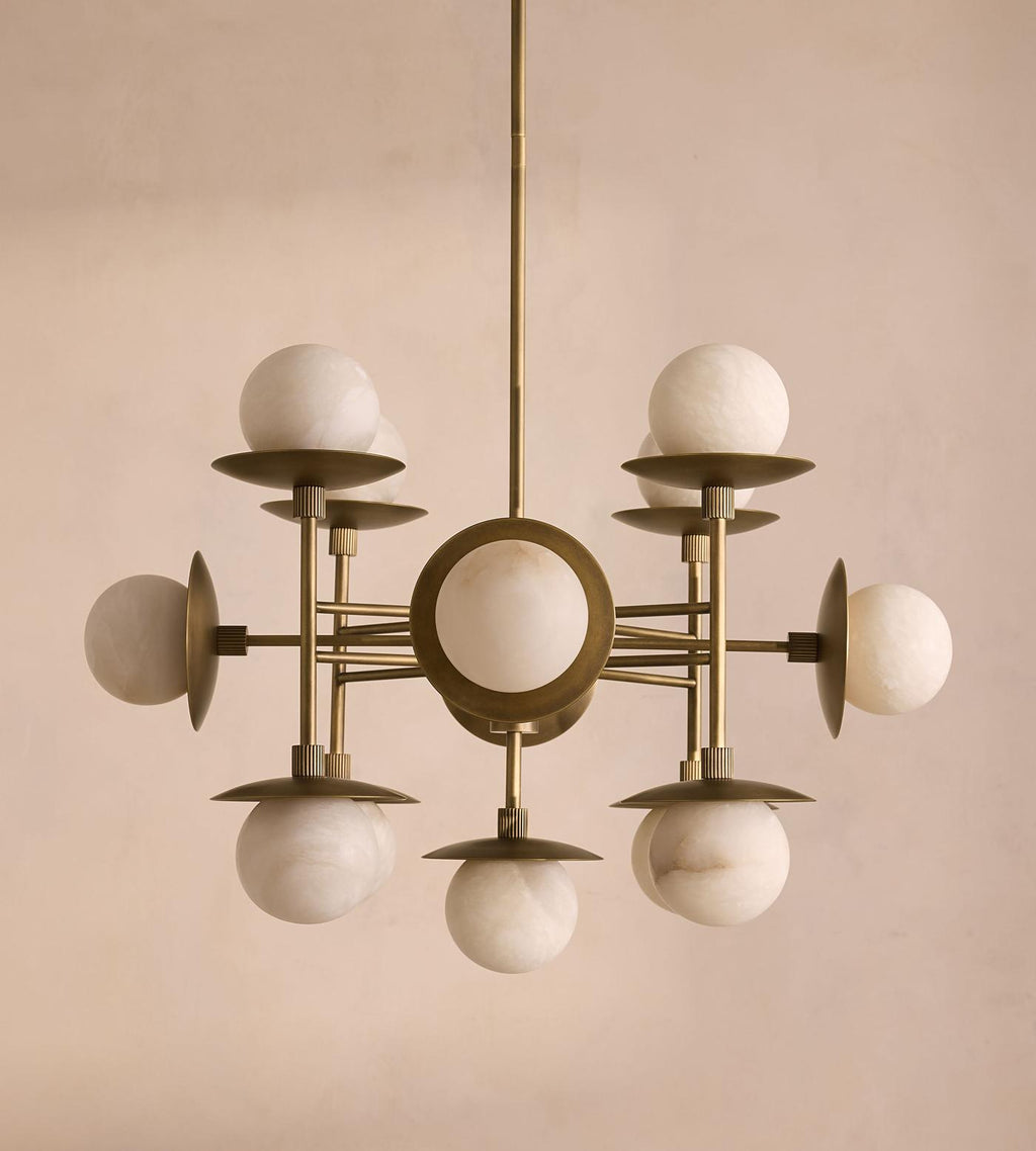 The Clérachic Xenon chandelier unlit on a plaster wall, cool white alabaster spheres set against aged brass discs.