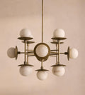 The Clérachic Xenon chandelier unlit on a plaster wall, cool white alabaster spheres set against aged brass discs.