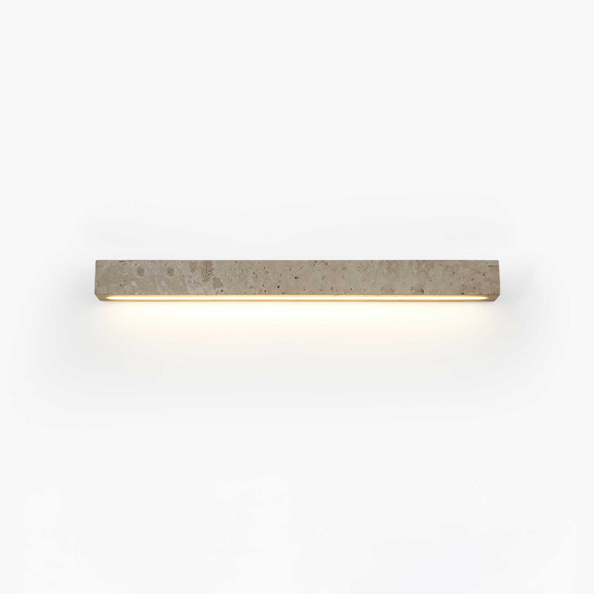 A slim pale travertine Clérachic wall light with its warm LED strip glowing below, shown on a white backdrop.