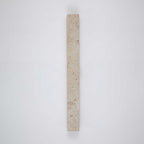 A vertical Clérachic wall light in pale travertine, shown unlit on a plain grey-blue wall.
