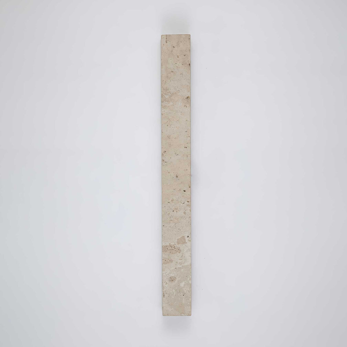 A vertical Clérachic wall light in pale travertine, shown unlit on a plain grey-blue wall.