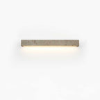 A short pale travertine Clérachic wall light with warm light beneath it, shown on a white backdrop.