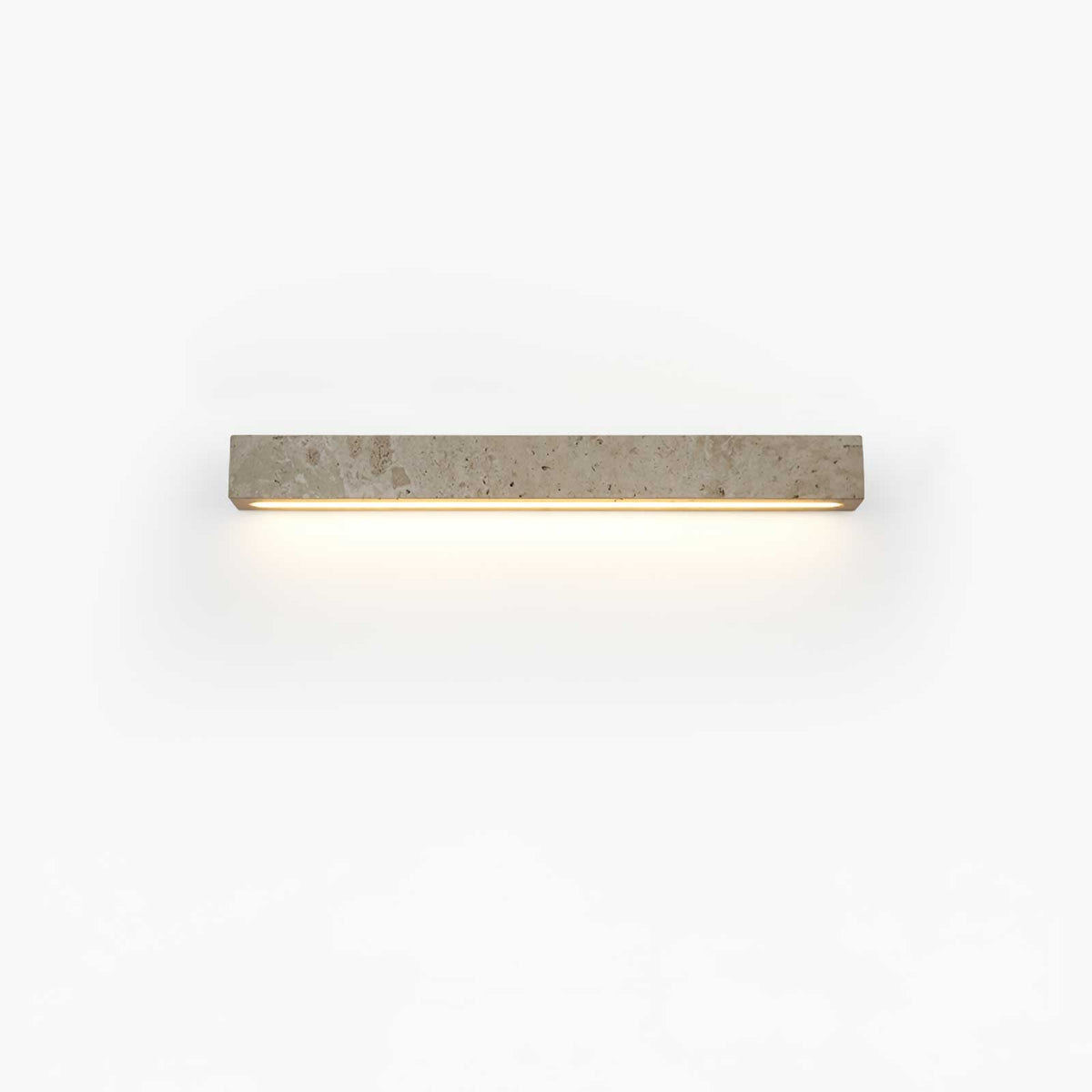 A short pale travertine Clérachic wall light with warm light beneath it, shown on a white backdrop.