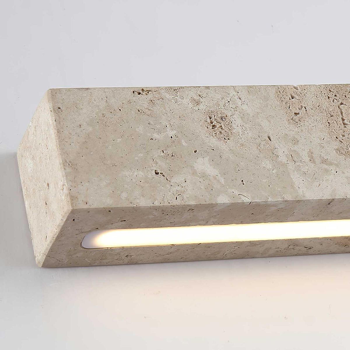 Close view of the end of this Clérachic travertine wall light, with its warm light glowing from a recessed slot.