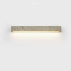A horizontal Clérachic wall light in speckled travertine with a warm glow beneath, on a pale backdrop.