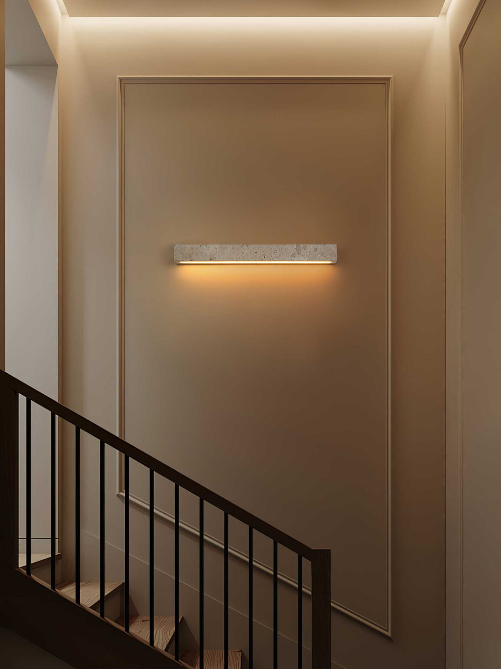 A Clérachic travertine wall light glows warm on a panelled stairwell wall beside a dark railing and cove lighting.