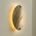 The Clérachic sconce lit from behind the stone, a warm halo spilling onto the wall along the lamp's left edge.