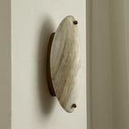 Clérachic wall lamp viewed from the side, the slim brass bracket lifting the stone clear of the wall it washes.