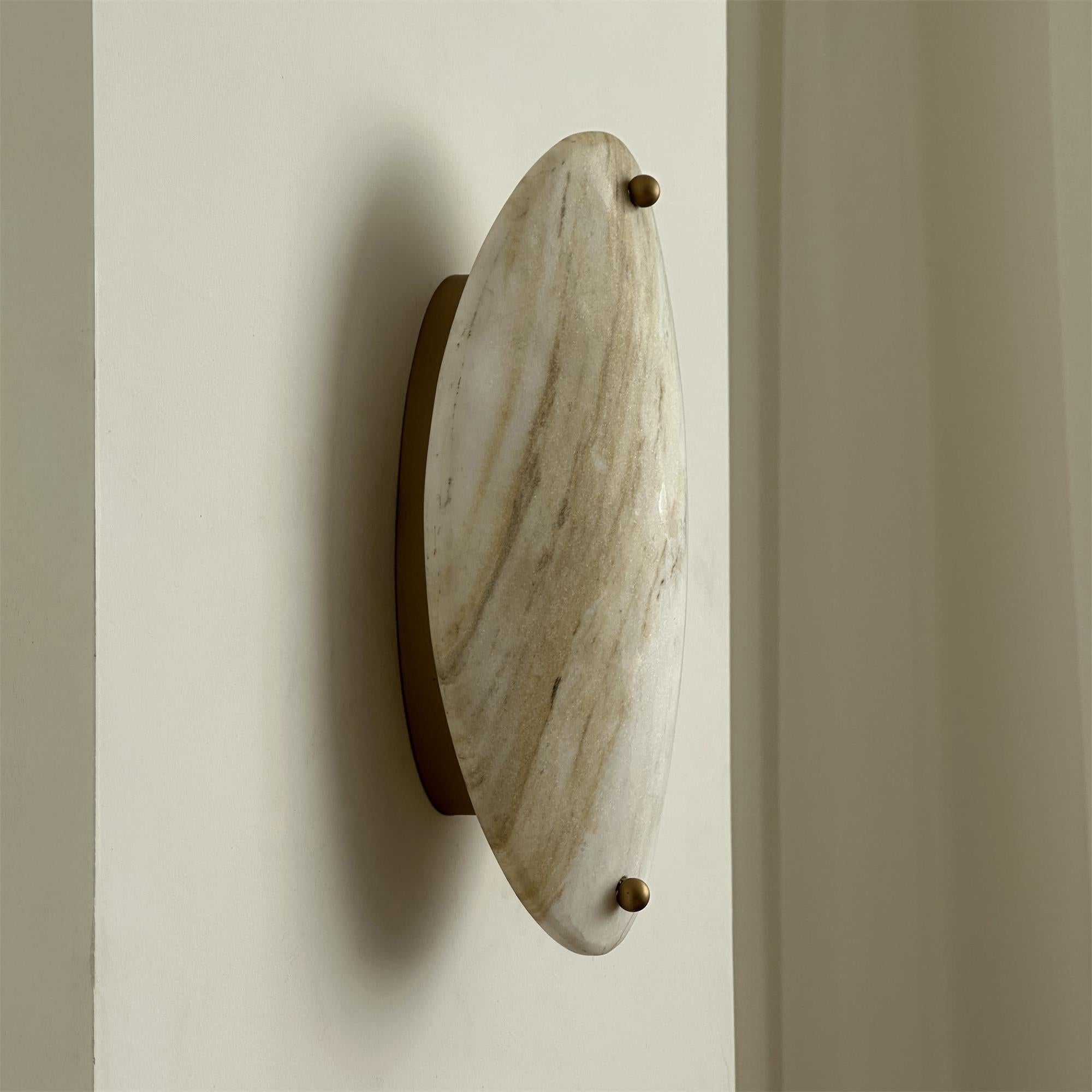 Clérachic wall lamp viewed from the side, the slim brass bracket lifting the stone clear of the wall it washes.