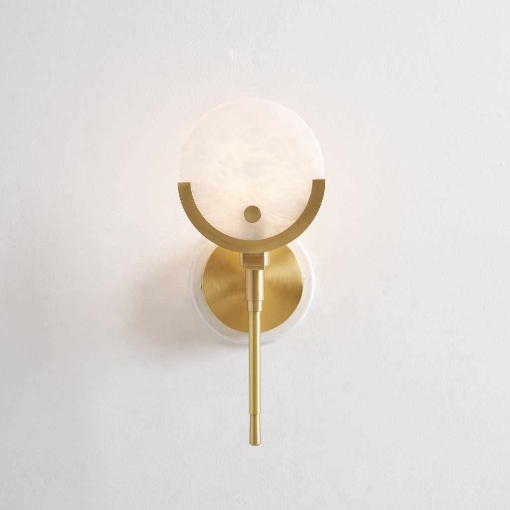 Front view of the Clérachic wall light, alabaster shade, brass crescent and circular backplate on a bare wall.