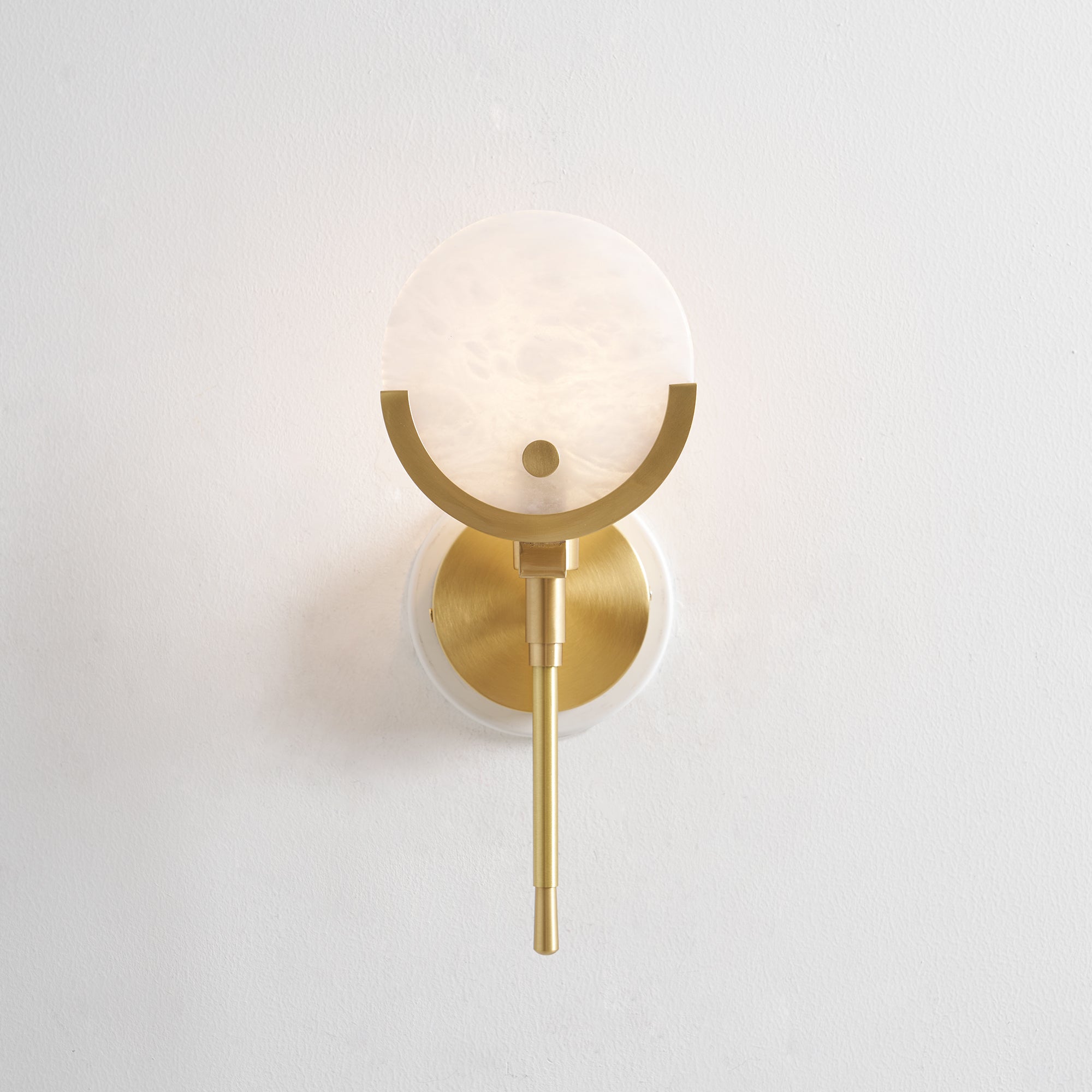 Front view of the Clérachic wall light, alabaster shade, brass crescent and circular backplate on a bare wall.