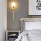 Clérachic wall light lit above a bedside shelf of books, in a soft grey bedroom with layered white linen.