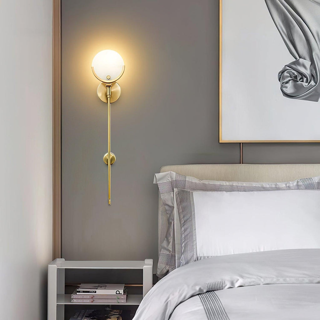 The Clérachic sconce lit in a grey bedroom corner, brass stem running down beside a gold-framed print.