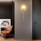 Clérachic sconce lit along a dim dressing corridor, brass warm against the grey wall and tan leather chair.