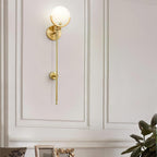 The Clérachic wall light lit on off-white panelling above a console, with a leafy plant to one side.