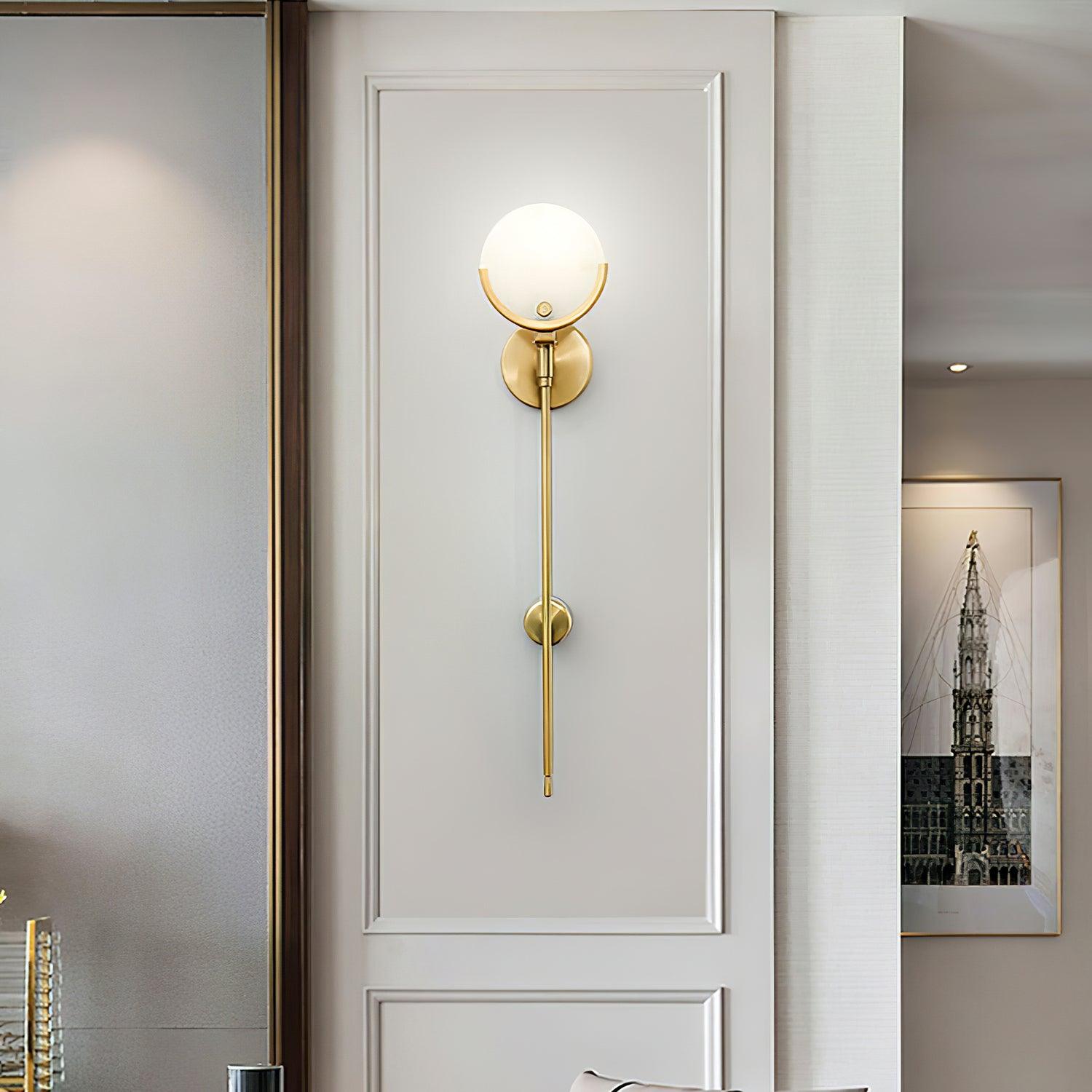 The Clérachic wall light lit on white panelling by a doorway, warm brass against the cool architrave.