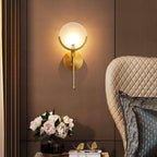 Clérachic sconce glowing on a warm bronze panelled wall, beside peonies and a quilted cream armchair.