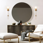 A pair of Clérachic wall lights framing a large round bronze mirror above a brushed metal sideboard.