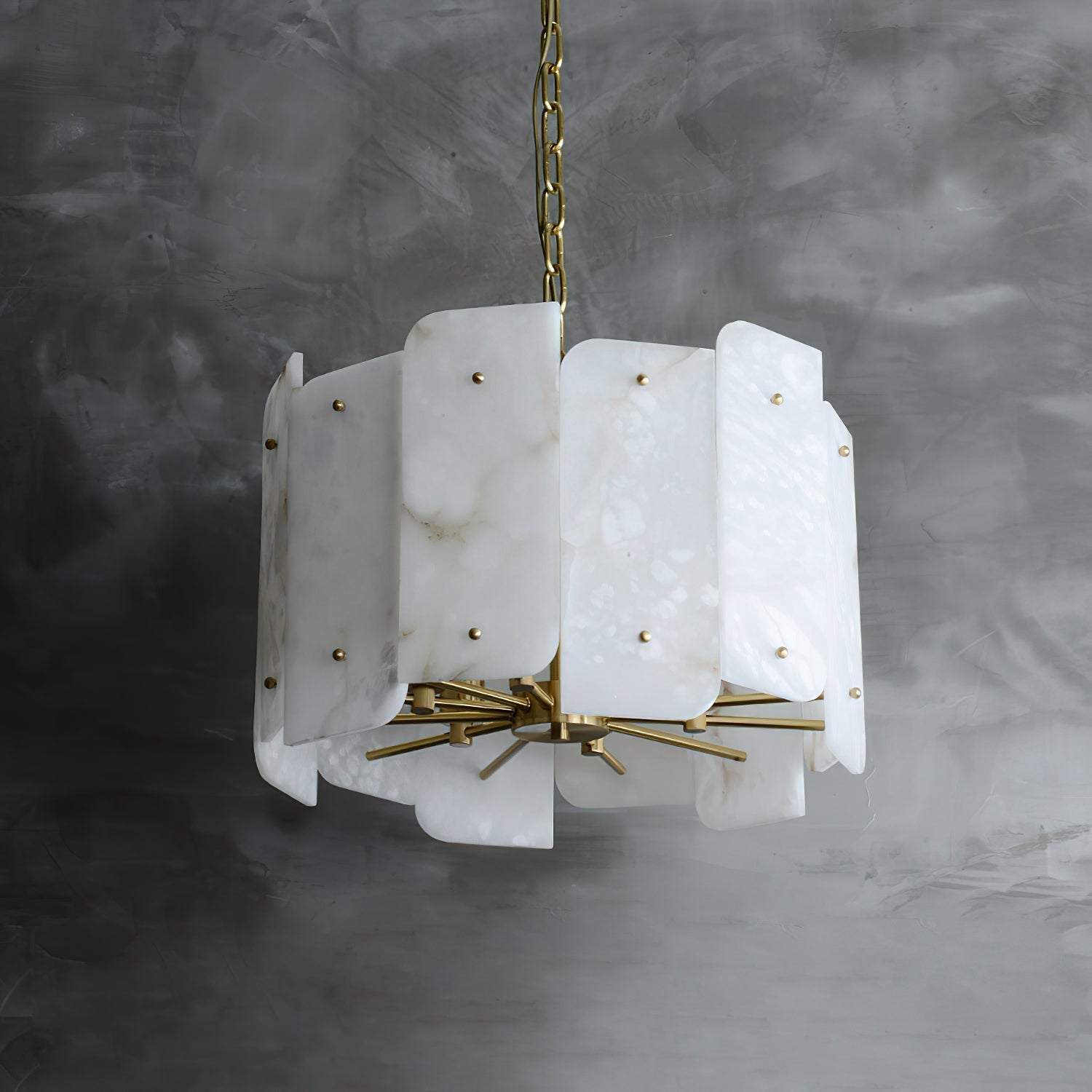 Unlit Clérachic Zoe alabaster chandelier on its brass chain against a raw concrete wall, every stone panel veined differently.