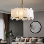 Clérachic Zoe alabaster chandelier lit above a pale sofa, with a round mirror and slatted wood panelling on the wall behind.