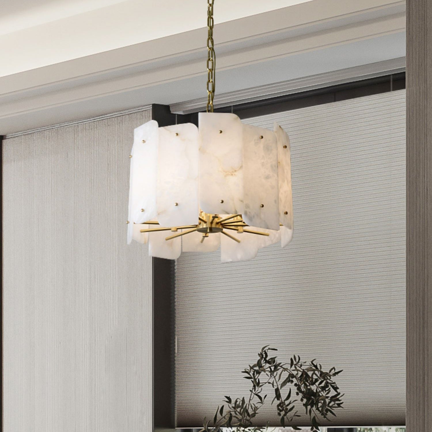 Clérachic Zoe alabaster chandelier on a brass chain beside a window dressed in woven grey blinds, olive branches below.