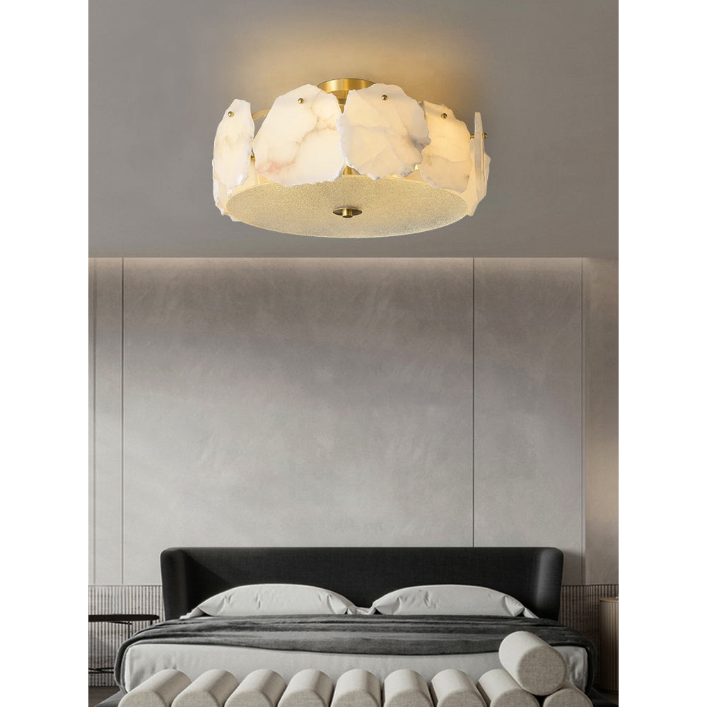 The Clérachic ceiling light above an upholstered panelled headboard, its alabaster ring warm against soft grey.