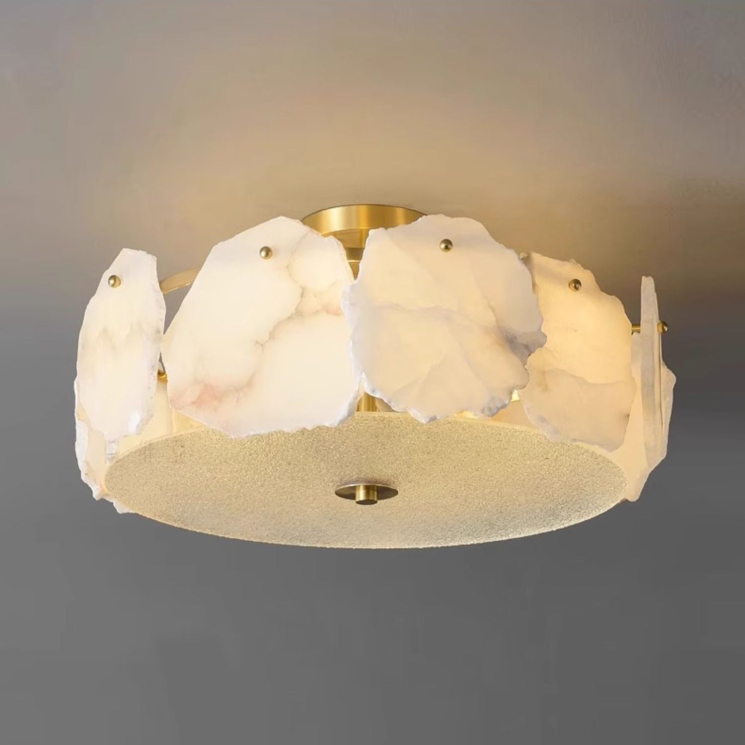 The Clérachic flush mount lit warm from beneath, brass hardware glinting between the pale stone panels.