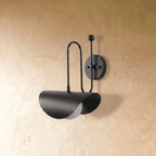 Clérachic curved-arm wall sconce in matte black, shown from a slightly closer studio angle on a plaster wall.