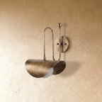 Clérachic curved-arm wall sconce in vintage brass, shown from a slightly closer studio angle on a plaster wall.
