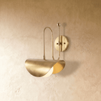 Clérachic curved-arm wall sconce in polished brass, shown from a slightly closer studio angle on a plaster wall.
