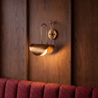 Clérachic vintage brass curved-arm wall sconce lit against a wood-panelled wall above a red velvet banquette.