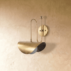 Clérachic curved-arm wall sconce in polished brass with a folded scallop shade, mounted on a plaster wall in studio light.