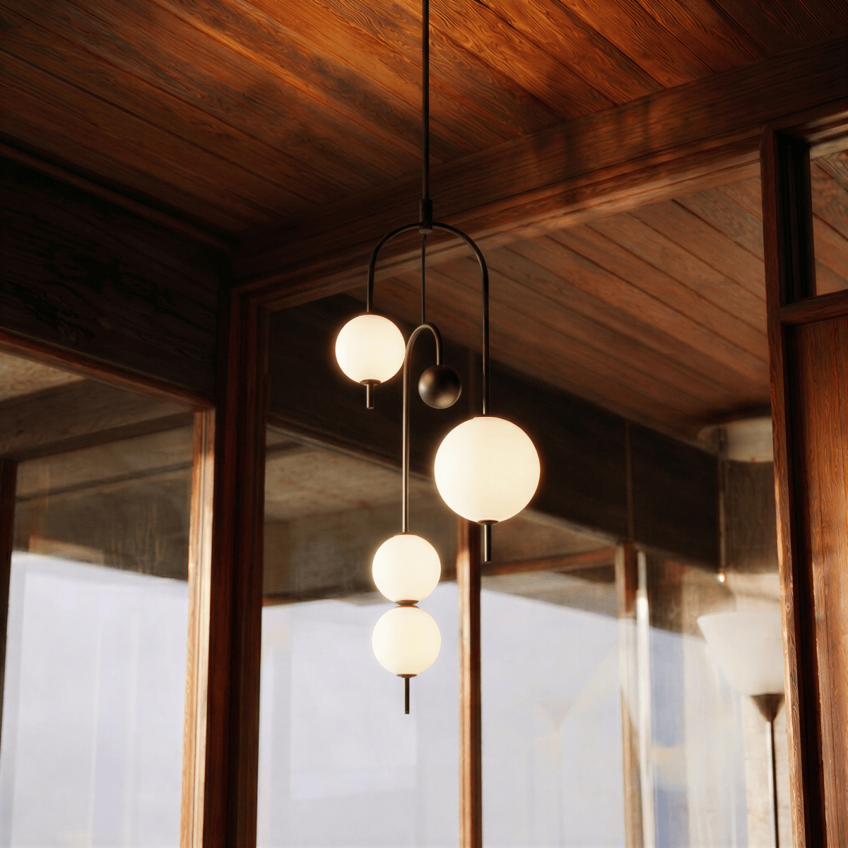 Clérachic pendant light in its four-globe build, its globes glowing beneath a timber plank ceiling with a glass wall behind.