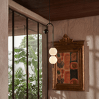 Clérachic pendant light dropping on a long bare rod beside a gilt-framed painting, its stacked opal globes set against a plaster wall.