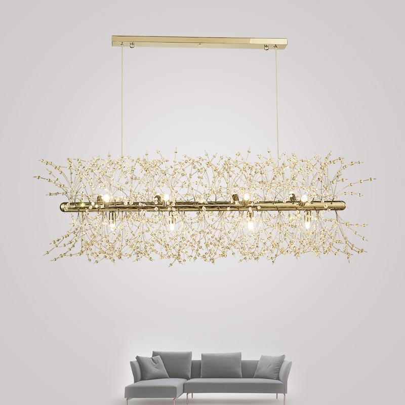 Product shot of a gold-finish rectangular bar pendant beside the edge of a grey sofa, a different Clérachic fixture from this chandelier.