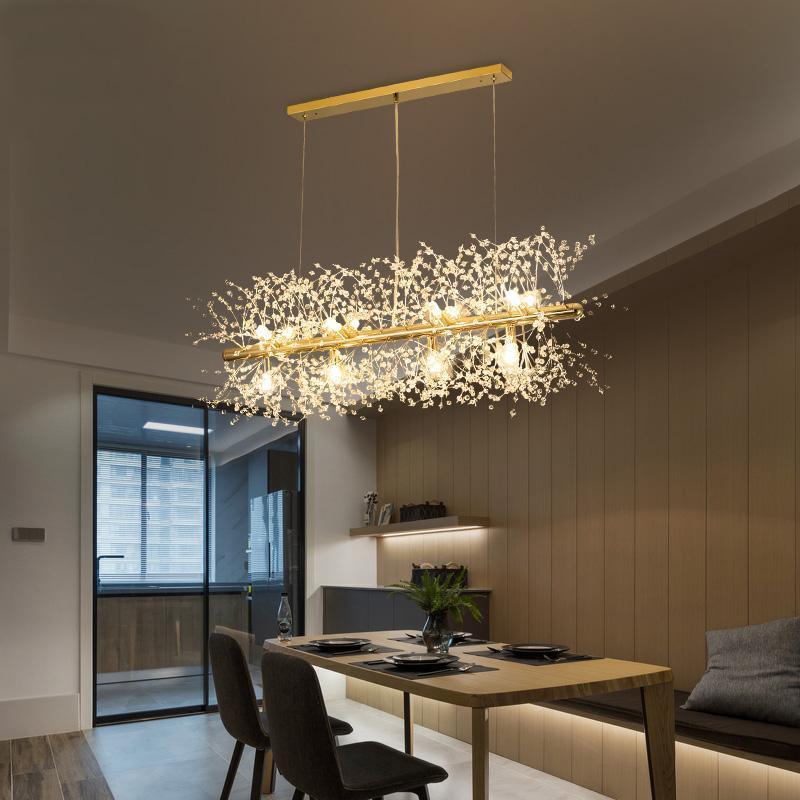 A rectangular gold-bar pendant hangs above a wood dining table near a sliding glass door, a different Clérachic fixture from this chandelier.