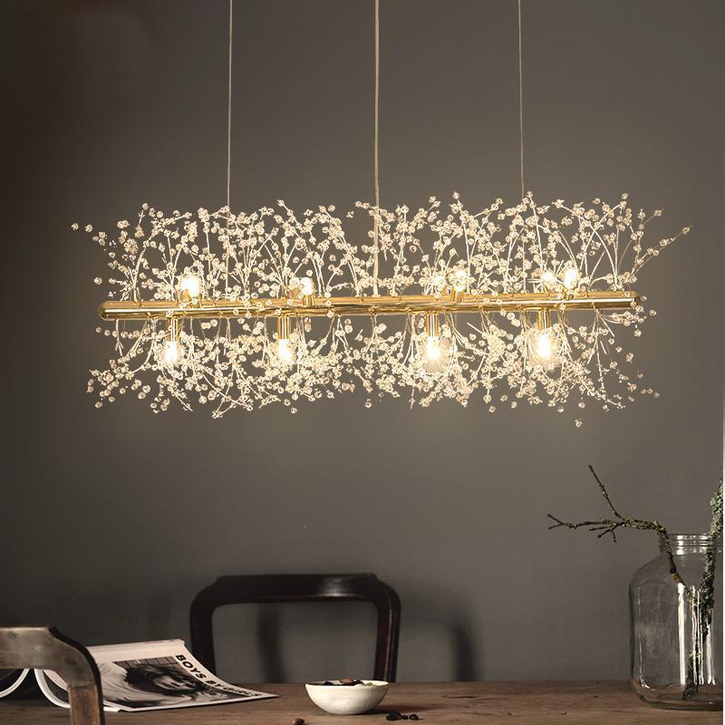A rectangular gold-bar pendant with crystal-tipped branches hangs above a dark wood table and chair, a different Clérachic fixture from this chandelier.