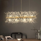 A rectangular gold-bar pendant with crystal-tipped branches hangs above a dark wood table and chair, a different Clérachic fixture from this chandelier.