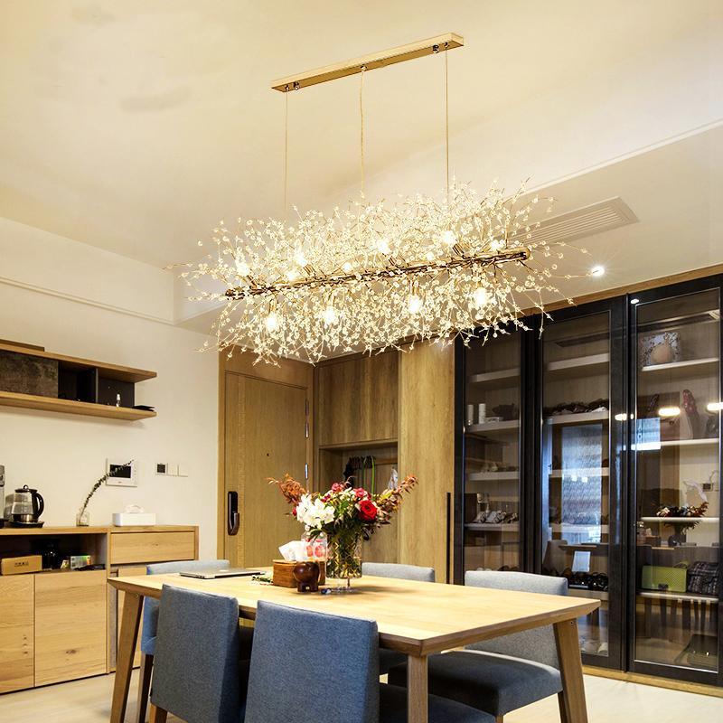 A rectangular gold-bar pendant with crystal-tipped branches hangs above a wood dining table in a kitchen with glass cabinets, a different Clérachic fixture from this chandelier.