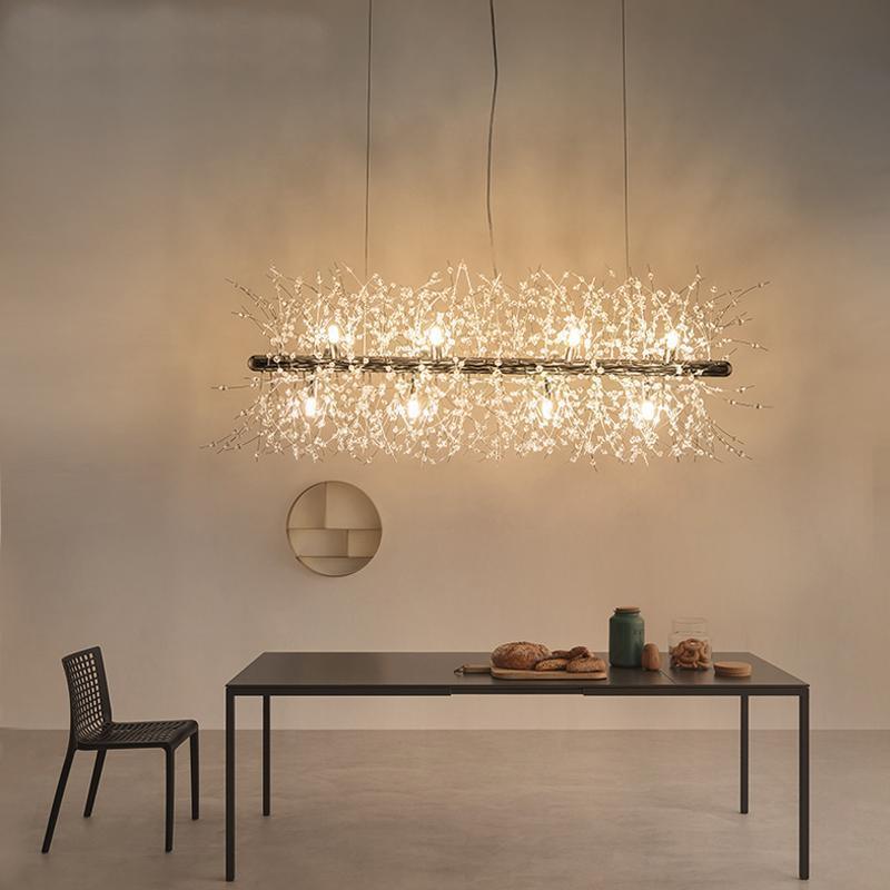 A rectangular gold-bar pendant with crystal-tipped branches hangs above a dark table beneath a round wall mirror, a different Clérachic fixture from this chandelier.