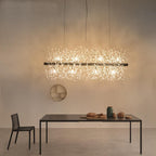 A rectangular gold-bar pendant with crystal-tipped branches hangs above a dark table beneath a round wall mirror, a different Clérachic fixture from this chandelier.