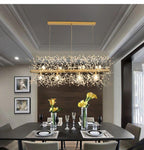 A rectangular gold-bar pendant hangs above a dark dining table set with a floral centrepiece, a different Clérachic fixture from this chandelier.