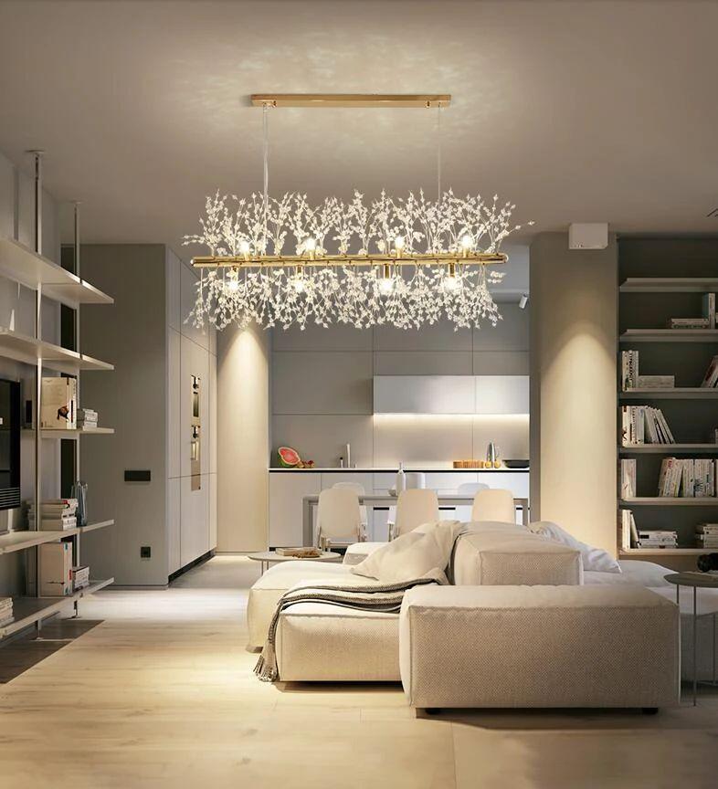 A rectangular gold-bar pendant hangs in a living room with open shelving and a cream sofa, a different Clérachic fixture from this chandelier.